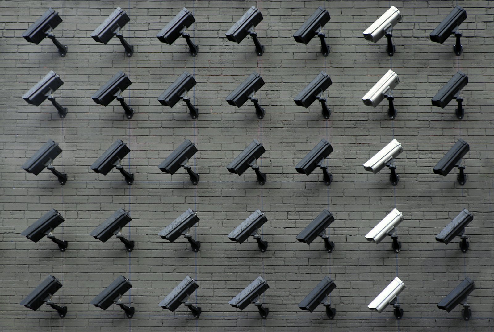 A dense grid of surveillance cameras mounted on a wall